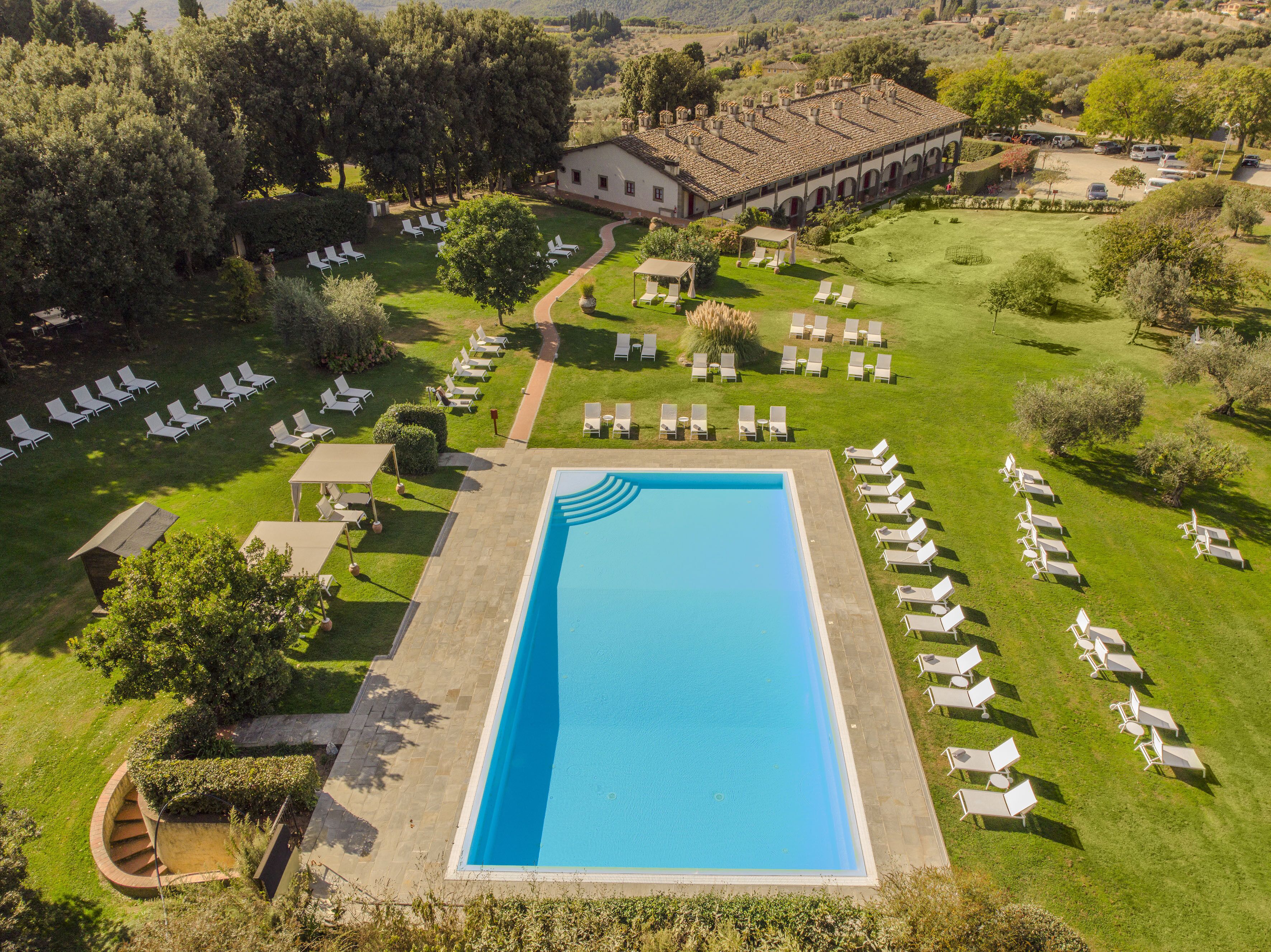 Vista aérea de un complejo turístico con una piscina rectangular rodeada de sillas de descanso y un edificio con tejado de baldosas.