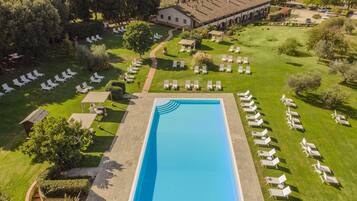 Vista aérea de un complejo turístico con una piscina rectangular rodeada de sillas de descanso y un edificio con tejado de baldosas.