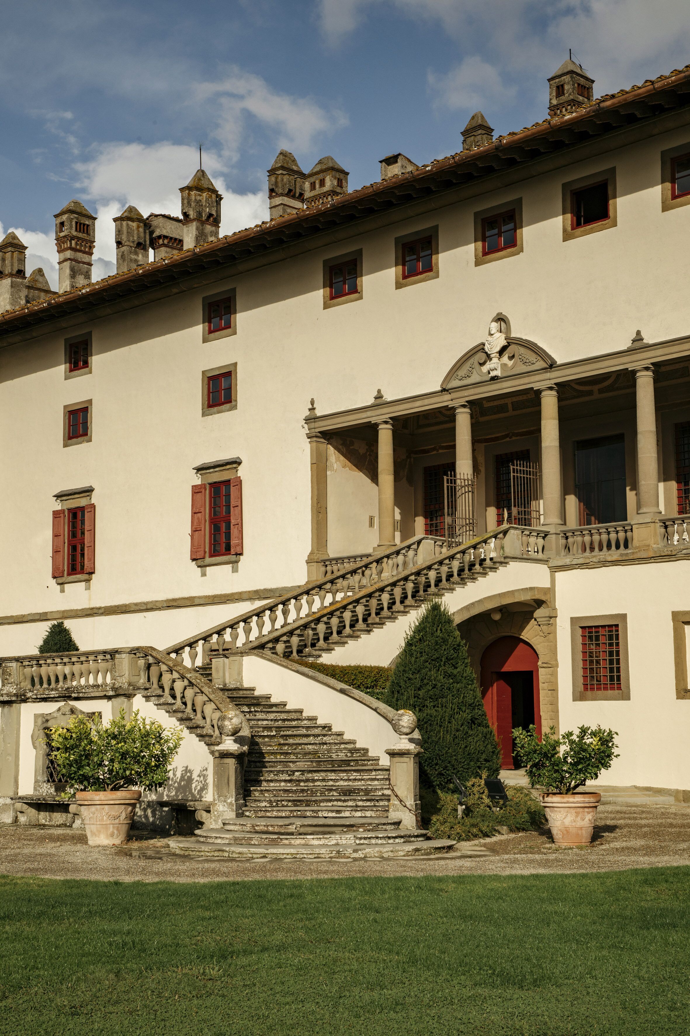 A historic building with a grand staircase, multiple windows, and a well-maintained lawn.