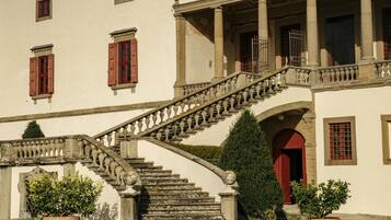A historic building with a grand staircase, multiple windows, and a well-maintained lawn.