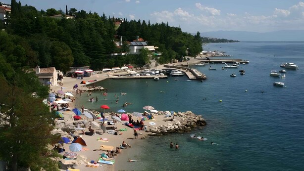 Une plage côtière aux eaux limpides, avec un rivage rocheux et plusieurs bateaux.