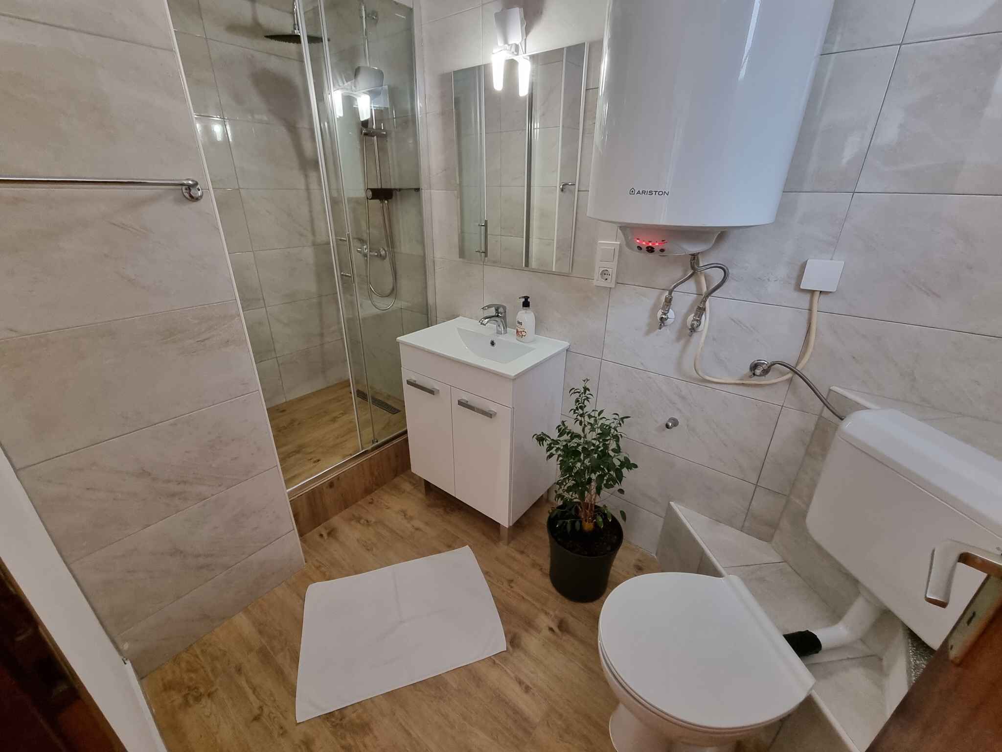 Un baño moderno con ducha envuelta en vidrio, un lavamanos blanco con espejo arriba y un inodoro.