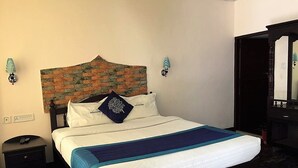 A neatly made bed with a blue and white bedspread, a wooden headboard, and a brick-patterned wall behind it. - Pavithram Homestay (Devikolam)