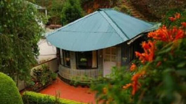 A small, round building with a blue roof, surrounded by lush greenery and a red pathway. - Pavithram Homestay (Devikolam)