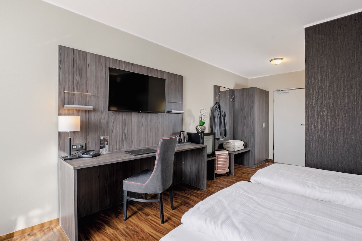 Ein Hotelzimmer mit einem Bett, einem Schreibtisch mit Stuhl, einem Flachbildfernseher, einer Lampe und einem Kleiderschrank.