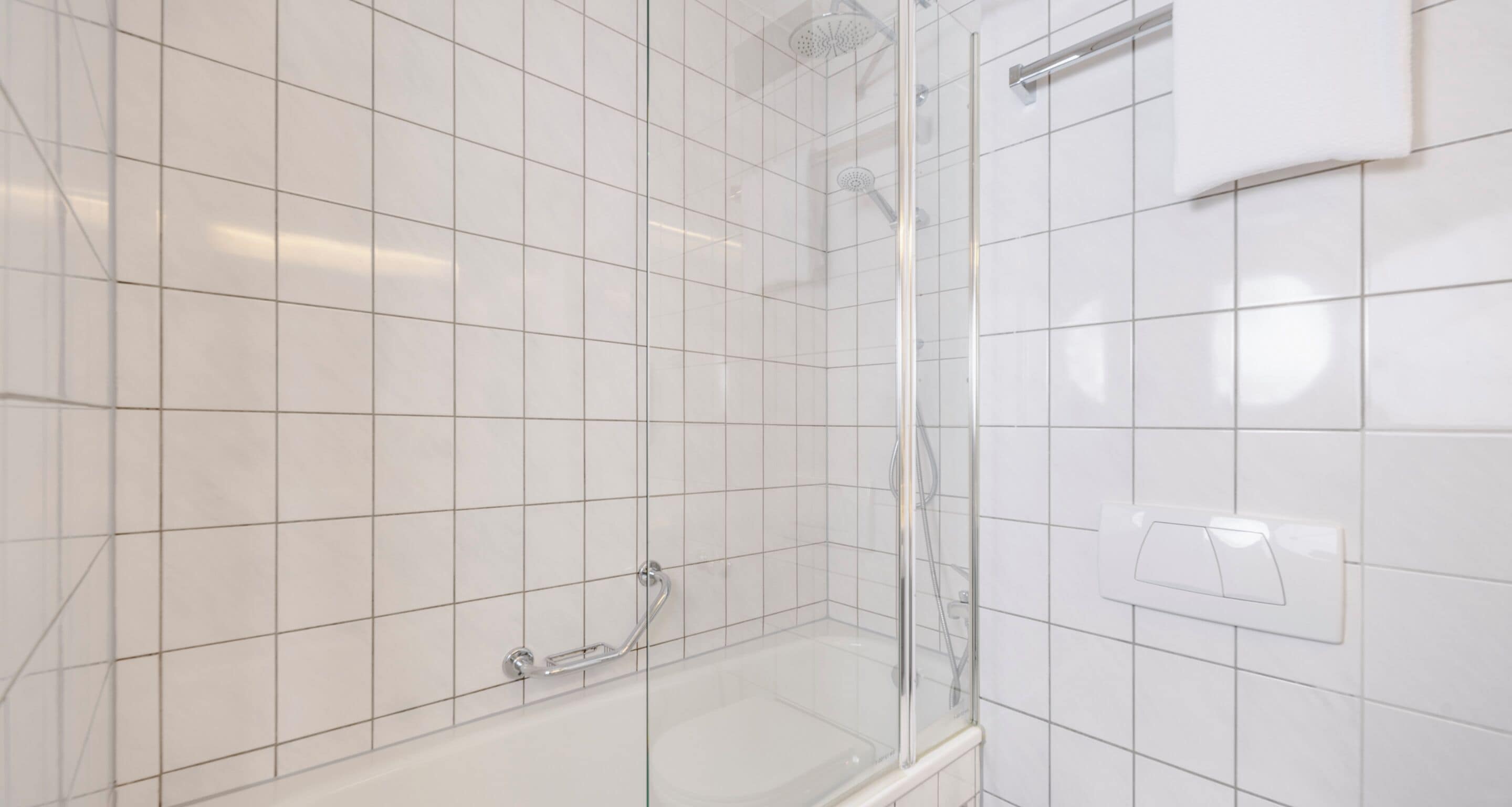 A bathroom with white tiled walls, a glass shower enclosure, and a bathtub with a handheld showerhead.