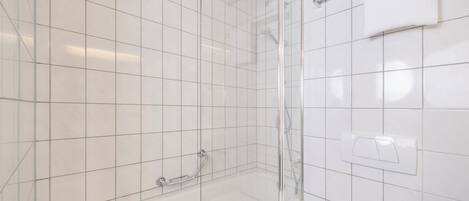 A bathroom with white tiled walls, a glass shower enclosure, and a bathtub with a handheld showerhead.