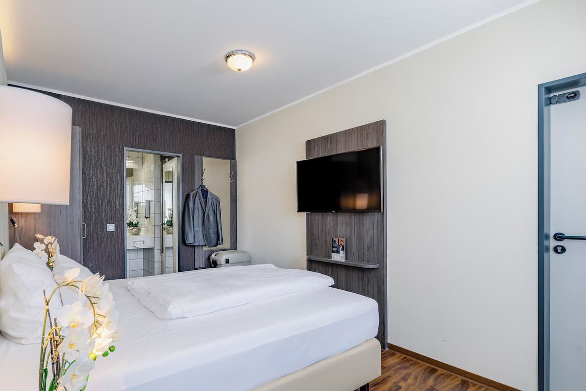 Ein Hotelzimmer mit einem Bett, einem an der Wand befestigten Fernseher, einem Spiegel, einer Tür und einer Lampe.