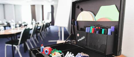 A black storage box with compartments containing various office supplies like pens, markers, and a toy.