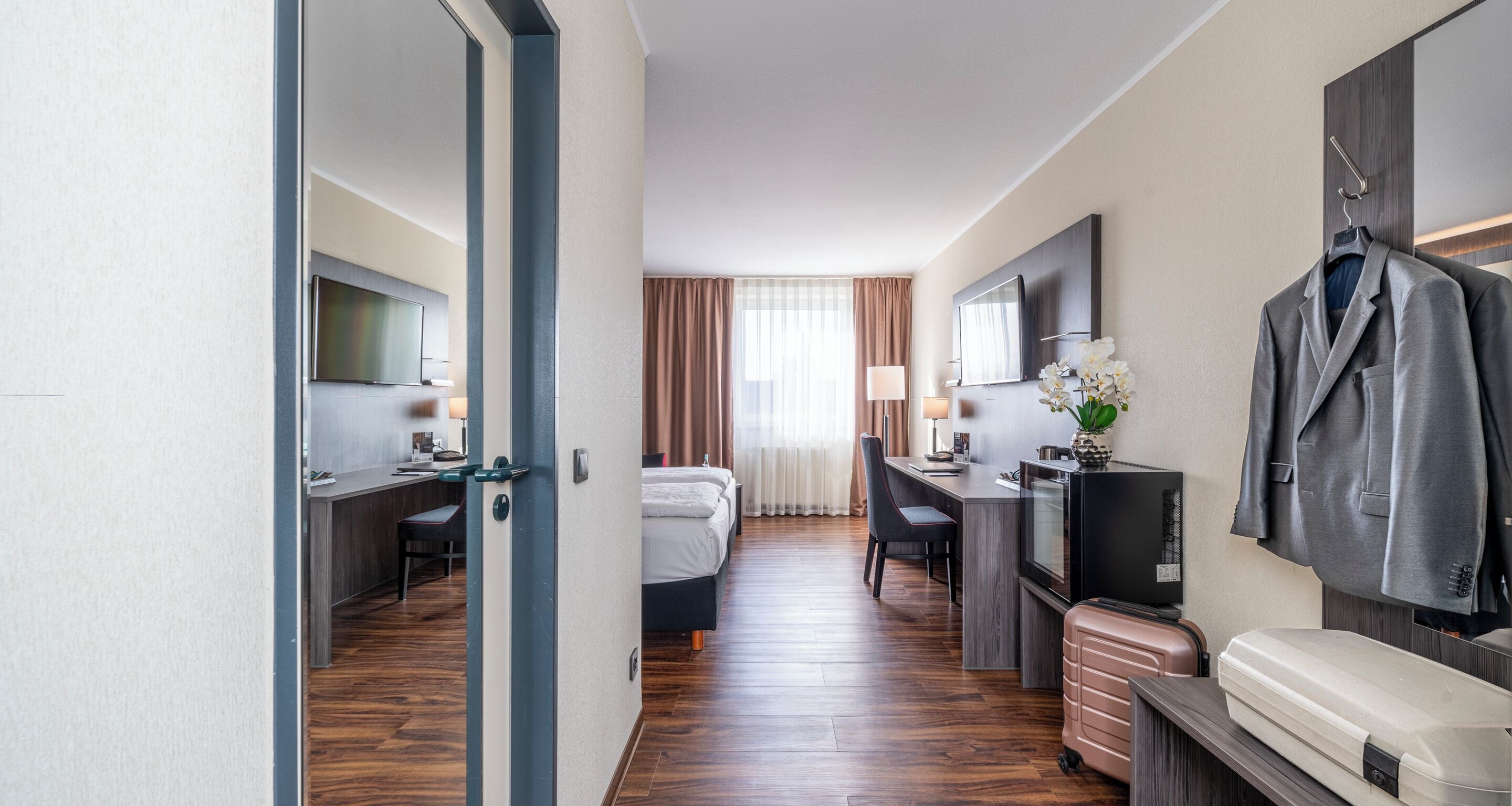 A hotel room with a bed, desk, TV, and a coat rack.