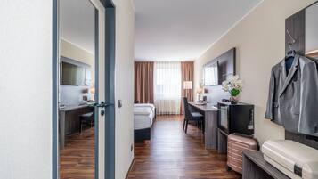 A hotel room with a bed, desk, TV, and a coat rack.