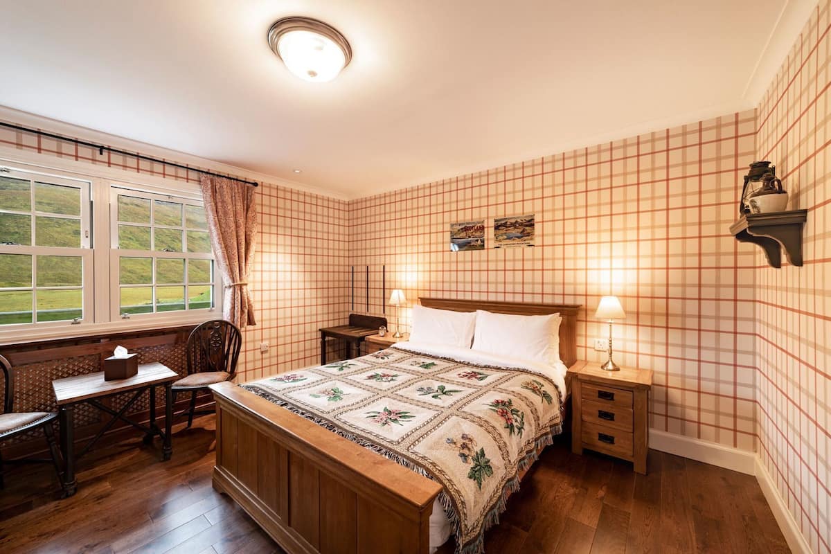 Un dormitorio con cama, mesitas de noche, escritorio, silla y ventana con cortinas.