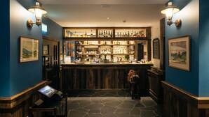 A bar area with a wooden counter, shelves of bottles, and framed pictures on the walls. -  The Cluanie Inn (Inverness)
