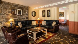 A cozy lounge area with a stone wall, two sofas with plaid upholstery, a coffee table, and a patterned rug. -  The Cluanie Inn (Inverness)