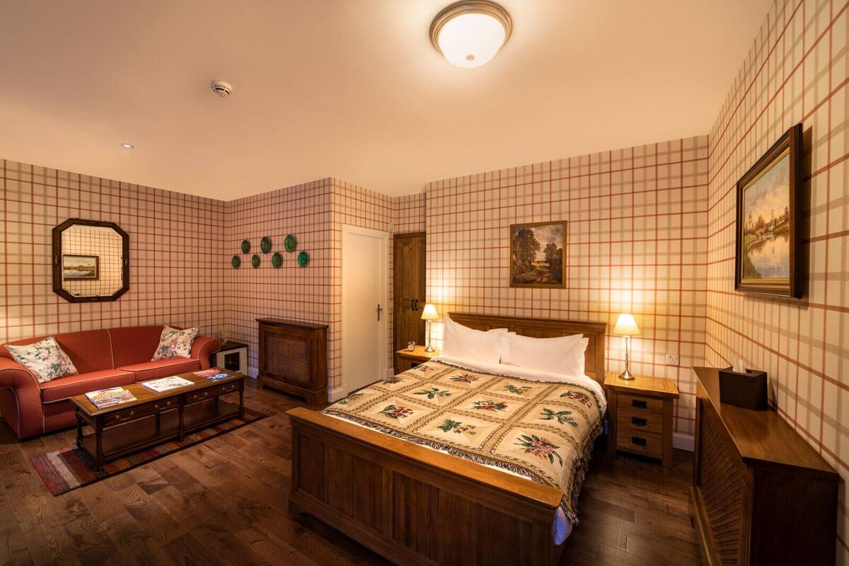 Un dormitorio ordenado con una cama de madera, un sofá rojo, una mesita pequeña y una mesita de noche con lámparas.