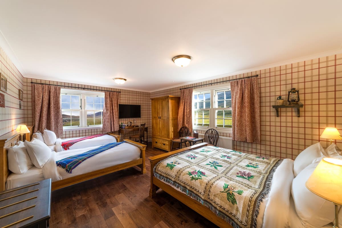 Habitación de hotel con dos camas, un escritorio, una silla, un televisor y una ventana con cortinas.