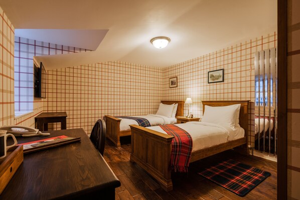 A hotel room with two wooden beds, a desk with a telephone, and a plaid rug.