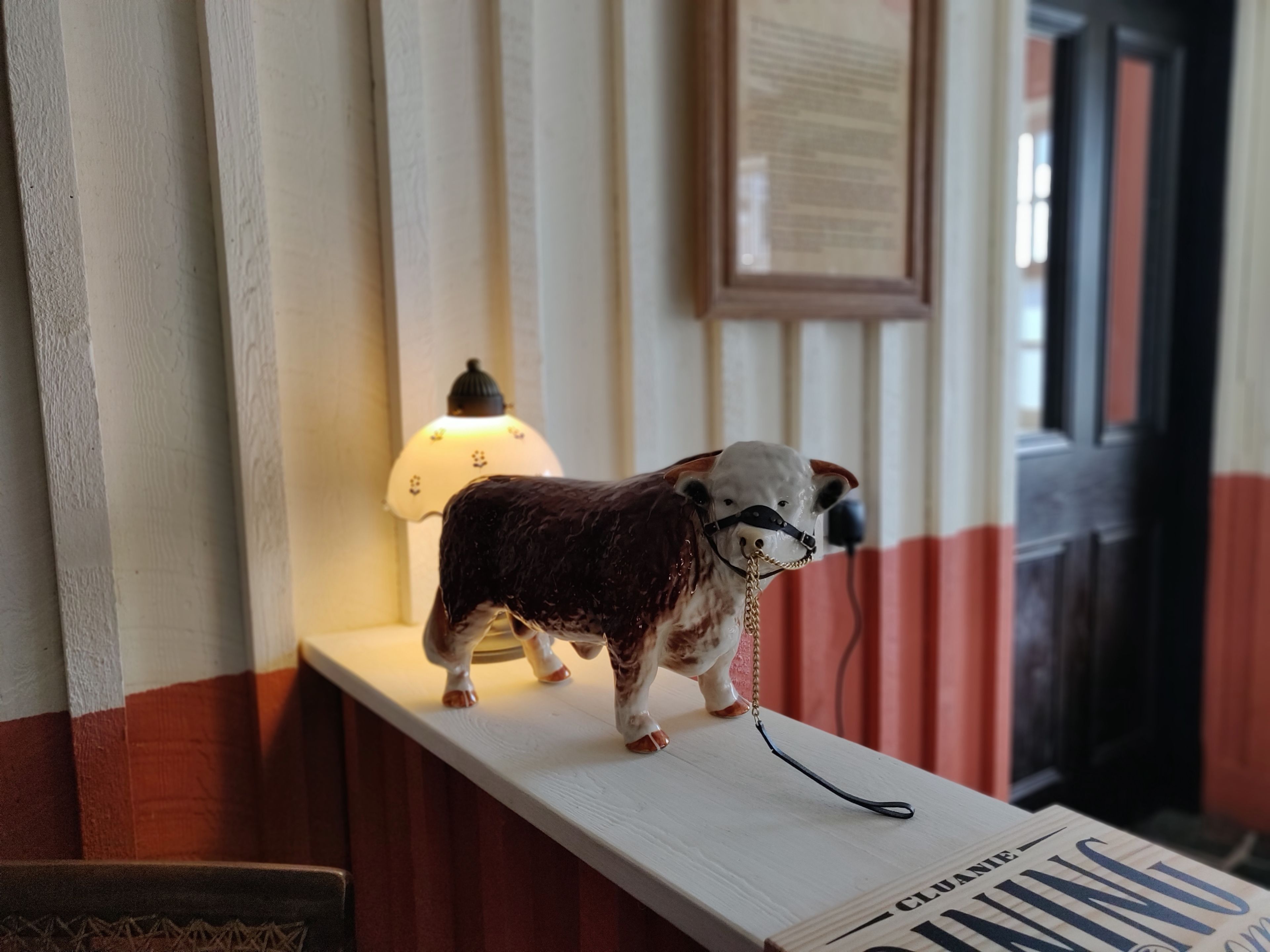 A cow figurine on a shelf with a lamp in the background.
