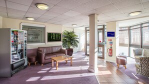 A lobby with a vending machine, a brown leather sofa, a wooden coffee table, a large potted plant, and a fire extinguisher mounted on the wall. - Redwings Lodge Solihull (Solihull)