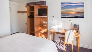 A hotel room with a bed, a wooden wardrobe with a television, a desk with a chair, and a sunset view on the wall. - Redwings Lodge Solihull (Solihull)