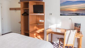 A hotel room with a bed, a wooden wardrobe with a TV, a desk with a chair, and a painting of a sunset. - Redwings Lodge Solihull (Solihull)