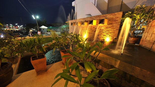 Un espacio exterior nocturno con fuente de agua, plantas en macetas y un muro de piedra.