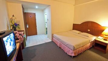 A hotel room with a bed, a television, a nightstand, and a door leading to another room.