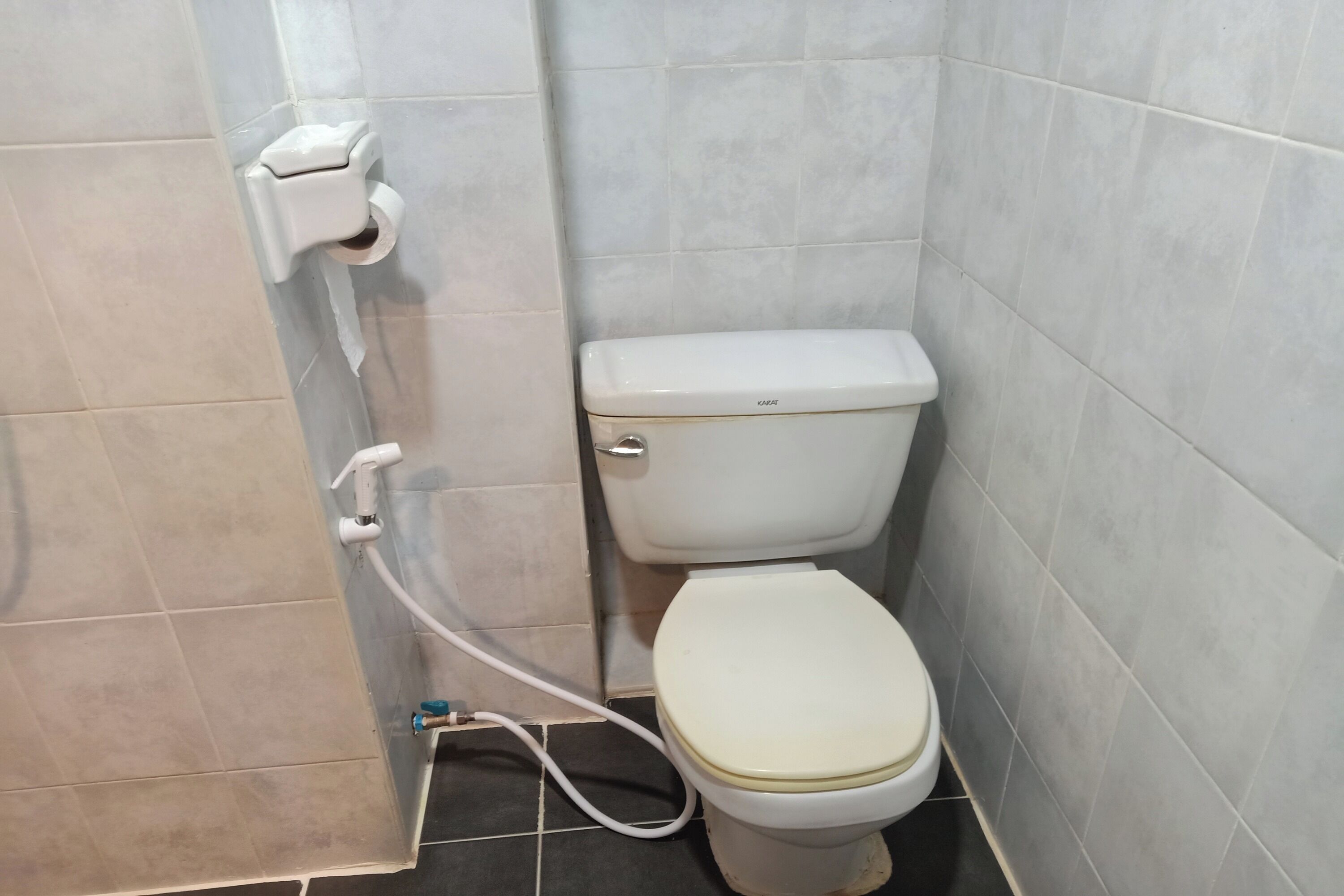 Een badkamer met een toilet, een papieren handdoekdispenser en een zichtbare pijp.