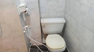 Een badkamer met een toilet, een papieren handdoekdispenser en een zichtbare pijp.