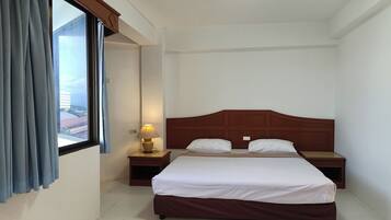 Een hotelkamer met een groot bed, twee nachtkastjes, een lamp en een raam met gordijnen.