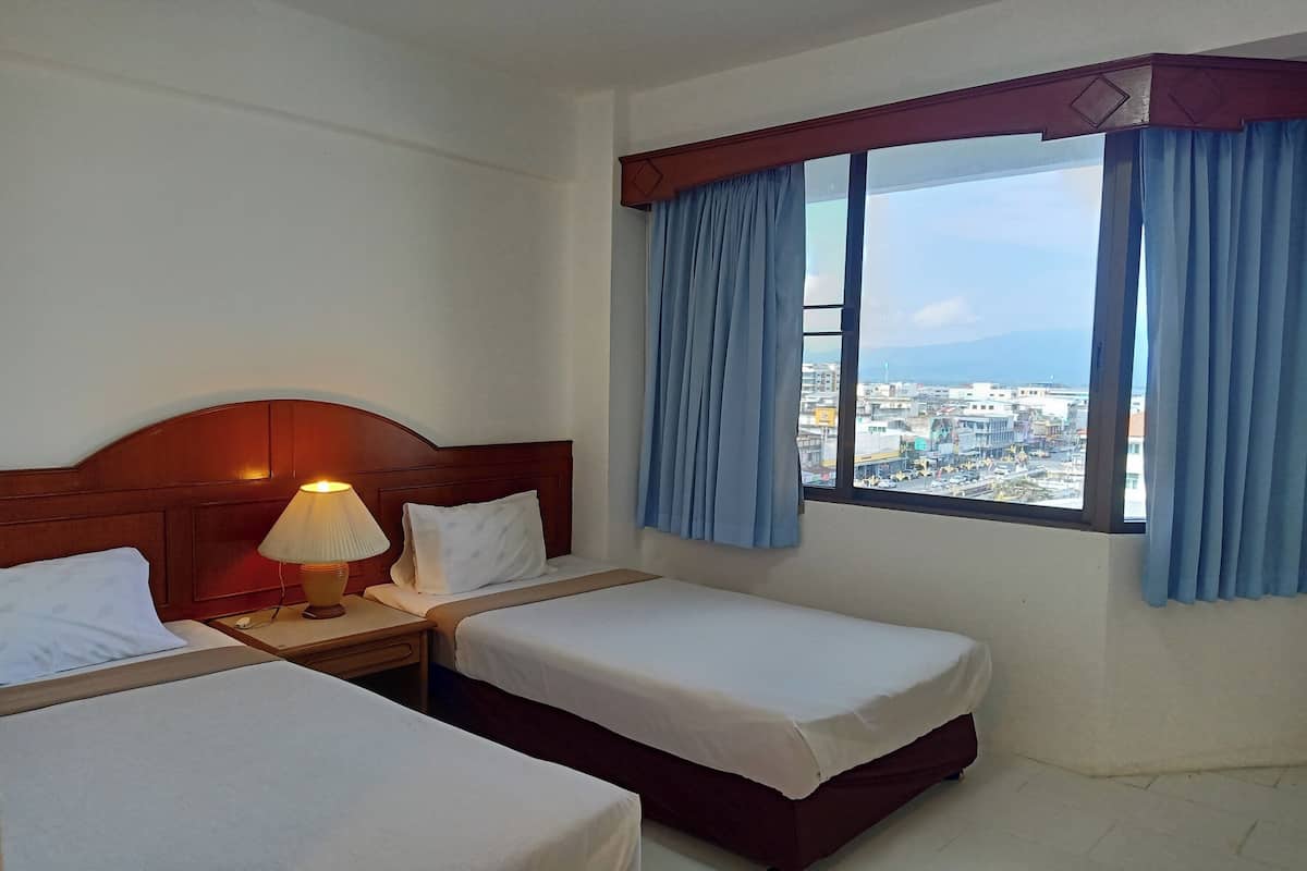 Una habitación de hotel con dos camas, una mesita de noche con lámpara y una ventana con cortinas.