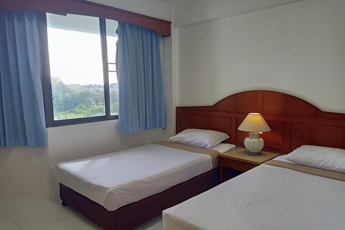 Una habitación de hotel con dos camas individuales, un cabecero de madera, una mesita de noche con lámpara y una ventana con cortinas azules.