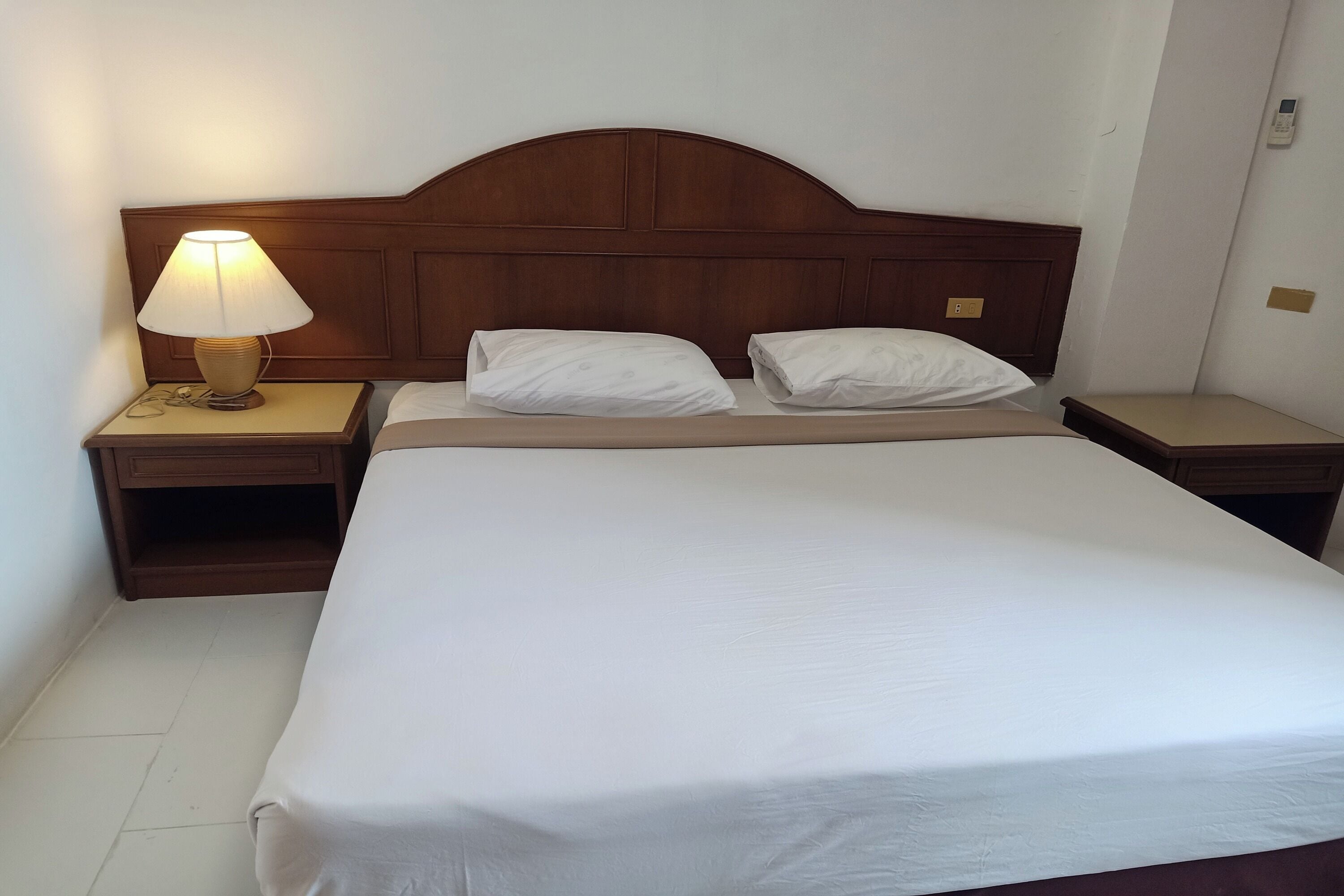 A neatly made bed with white linens, a wooden headboard, and two bedside tables with lamps.