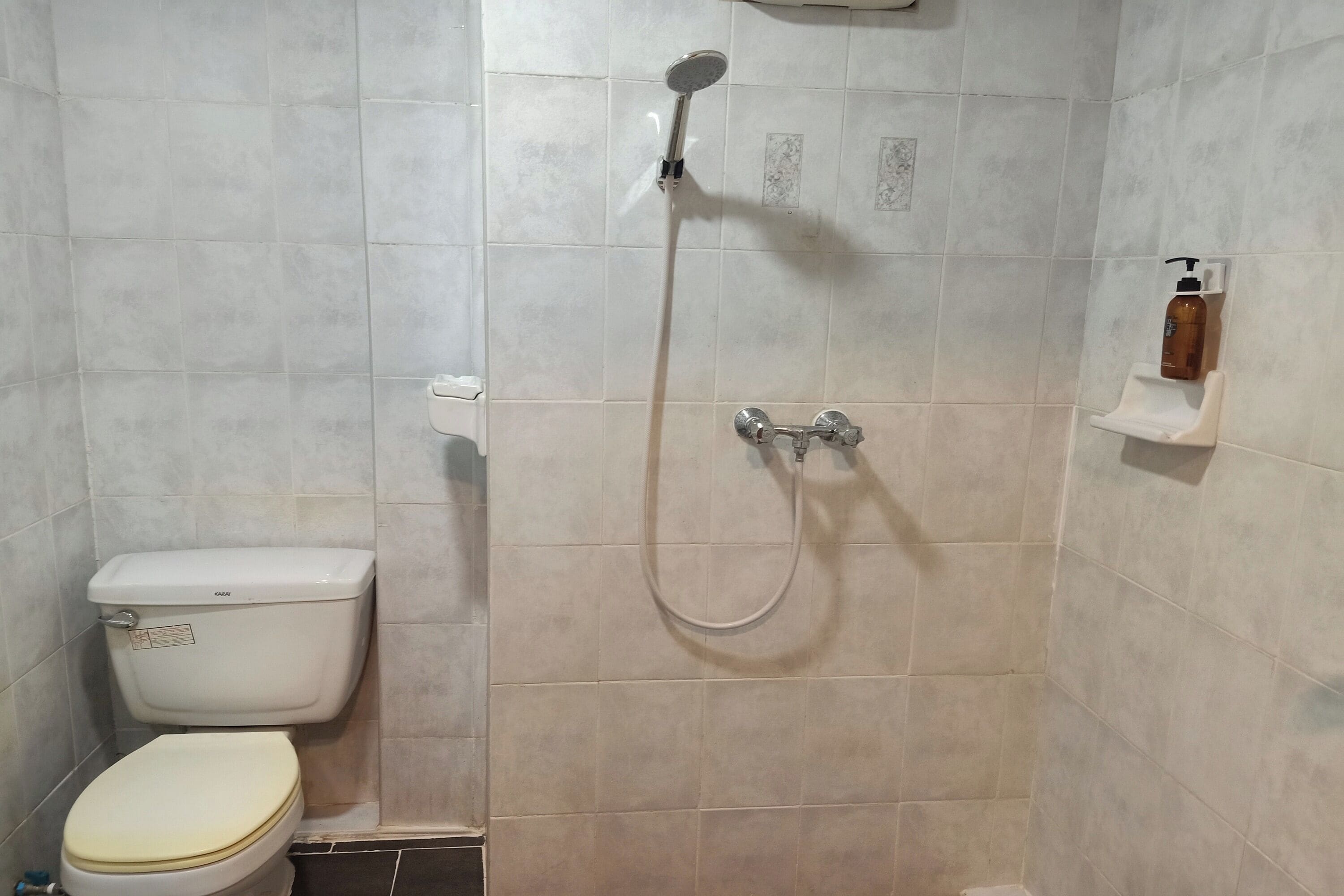 Um banheiro pequeno revestido com azulejos, com vaso sanitário, chuveiro e um dosador de sabonete na parede.