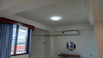 Una habitación con ventana, aire acondicionado, un espejo redondo y una mesa con sillas.