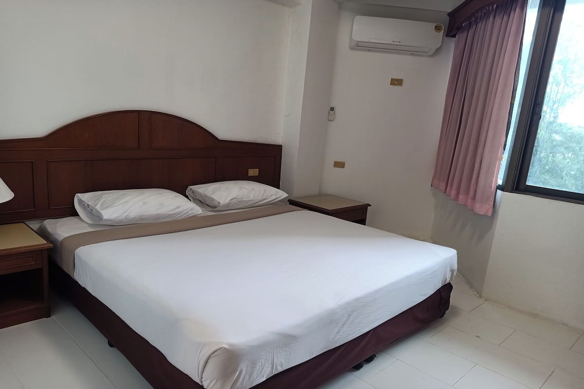 Una cama bien tendida con ropa blanca, un cabecero de madera y una mesita de noche con lámpara.