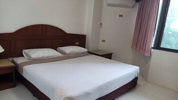Una cama bien tendida con ropa blanca, un cabecero de madera y una mesita de noche con lámpara.