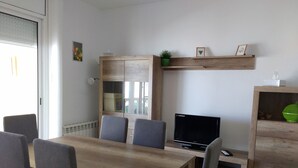 A modern living room with a wooden dining table, two grey chairs, a flat-screen TV, a wooden cabinet with a green plant, and a framed picture on the wall. - Villa with private pool for 7 people, 4000m from the beach, private pool (L'Ametlla de Mar)