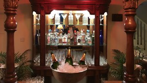 A bar area with a wooden bar counter, bottles of alcohol, and glasses. - Inch Schoolhouse - Event Residence (Downpatrick)