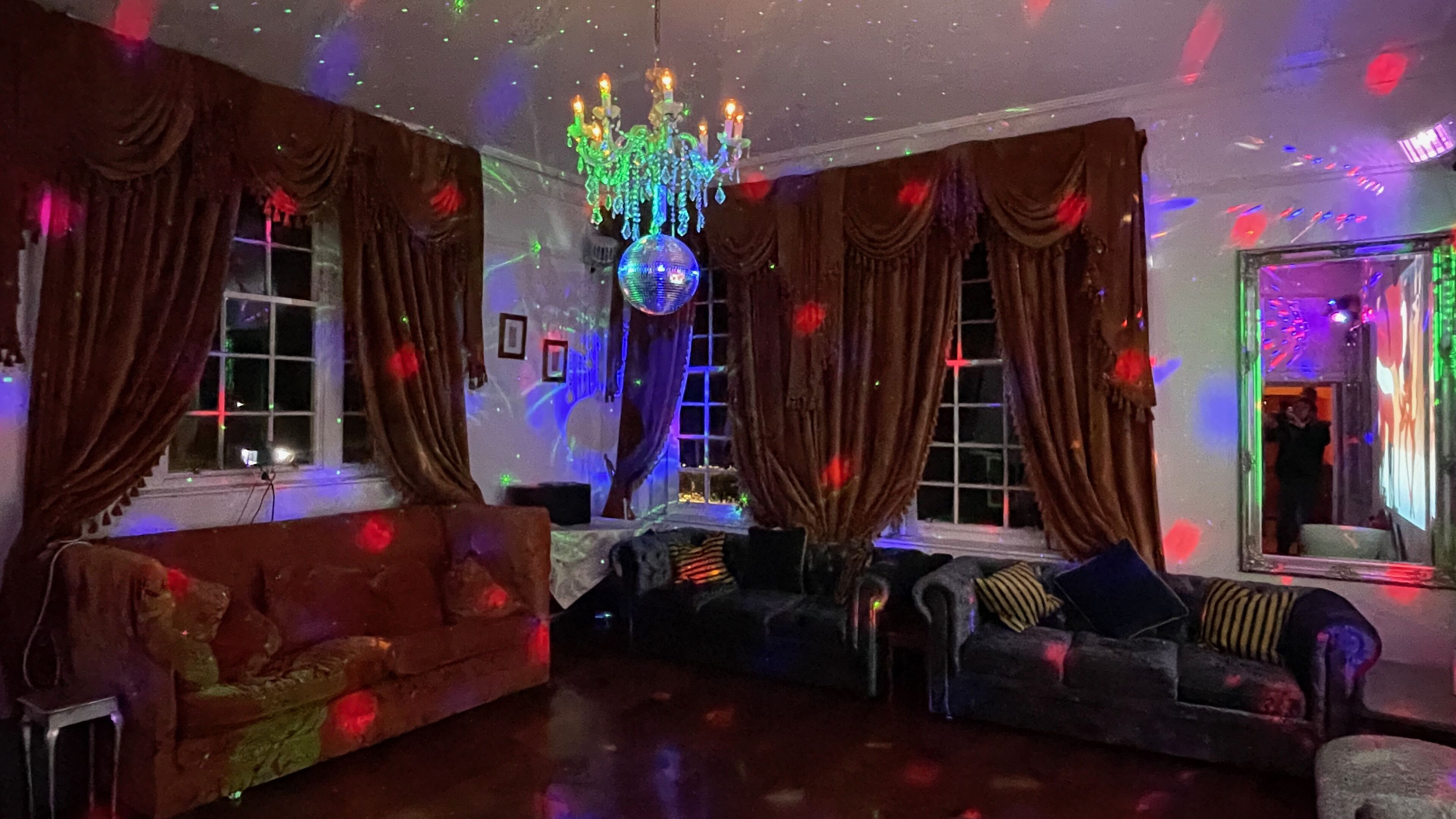 A room with a chandelier, two sofas, and draped curtains.