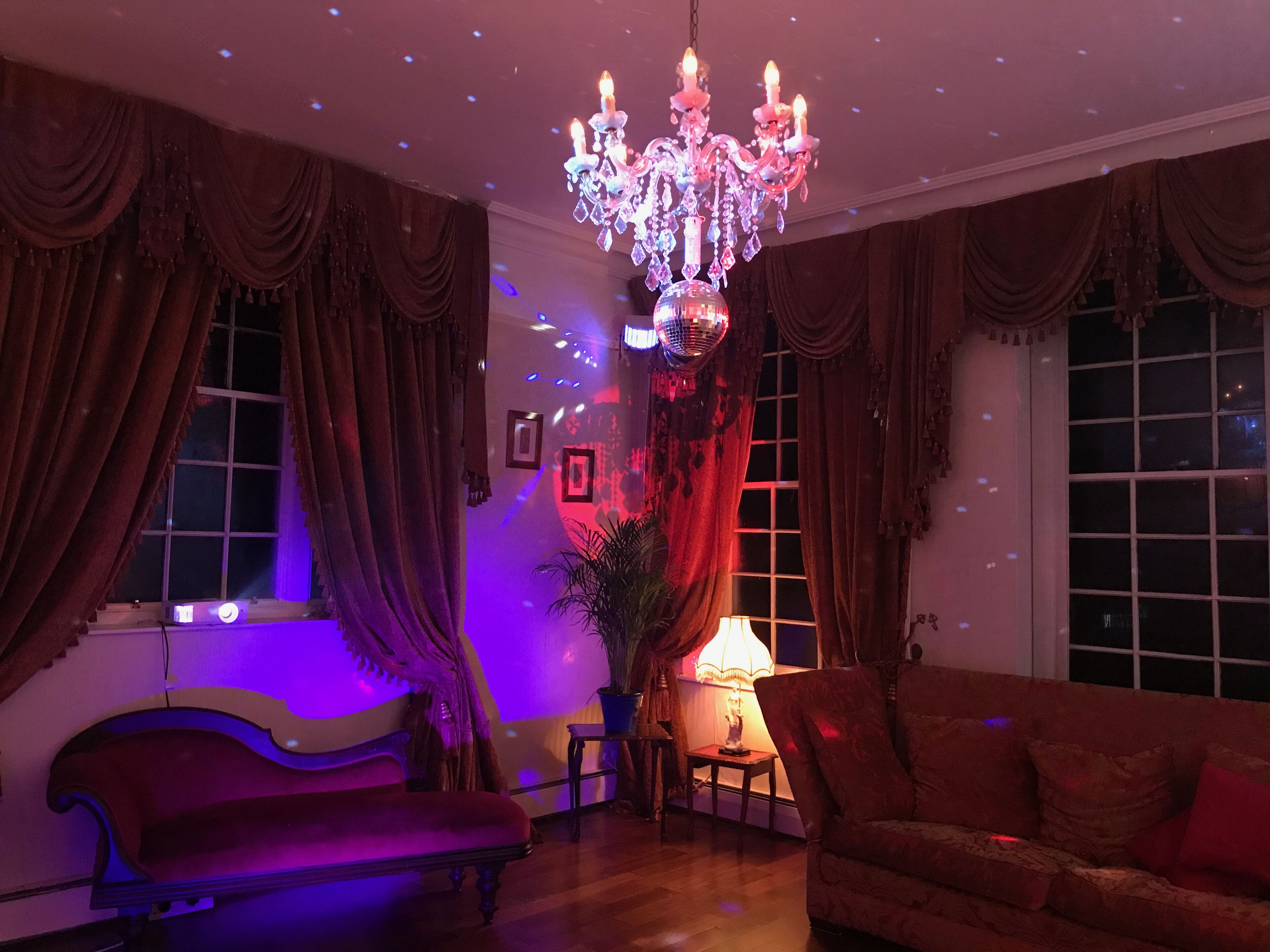 A room with a chandelier, curtains, a sofa, and a lamp.