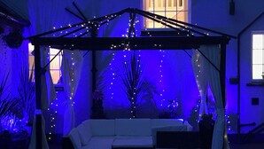 A covered outdoor seating area with a white sofa, string lights, and curtains. - Inch Schoolhouse - Event Residence (Downpatrick)