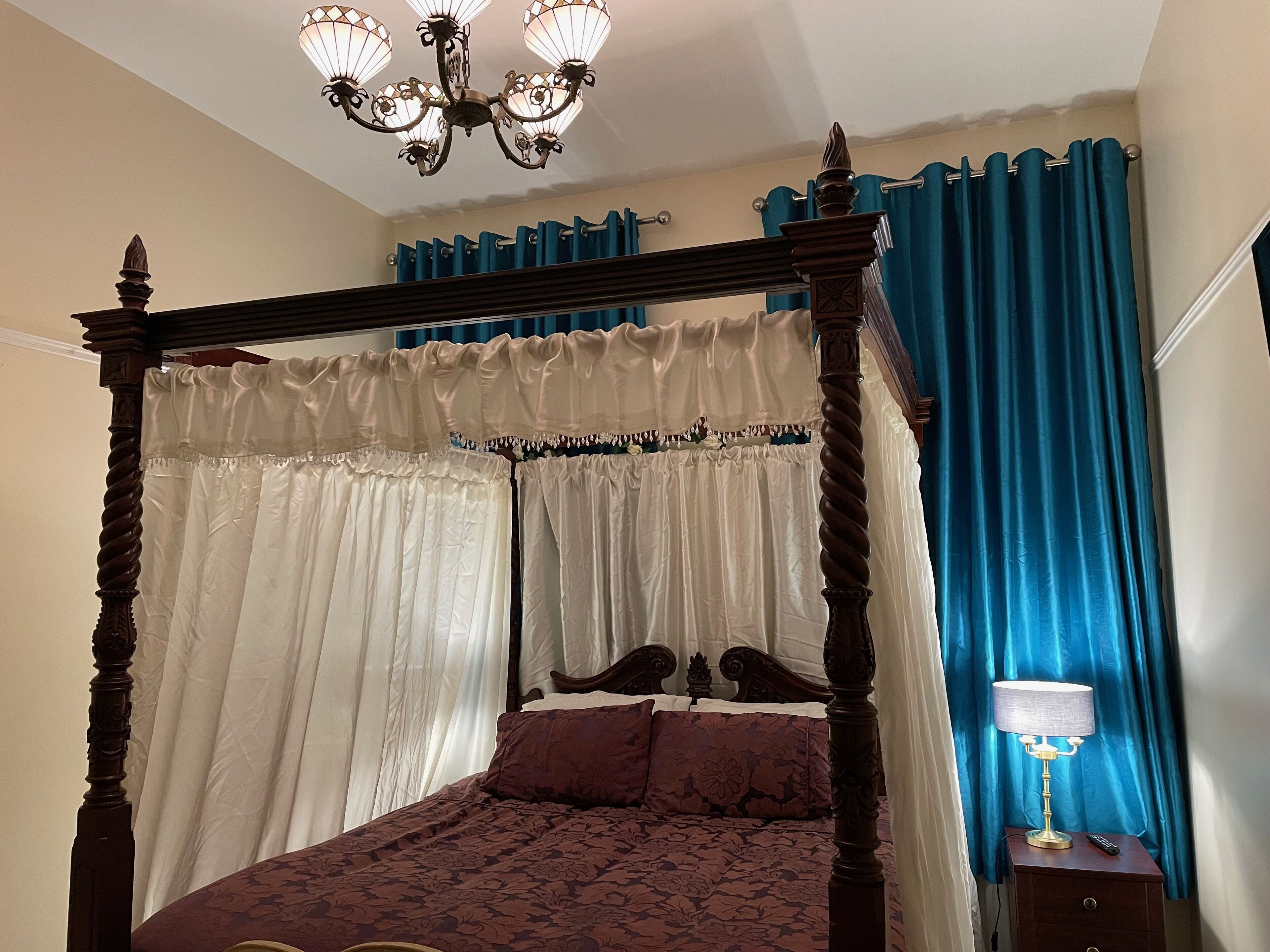 Una cama con dosel con cortinas blancas y azules, un candelabro y una mesita de noche con una lámpara.