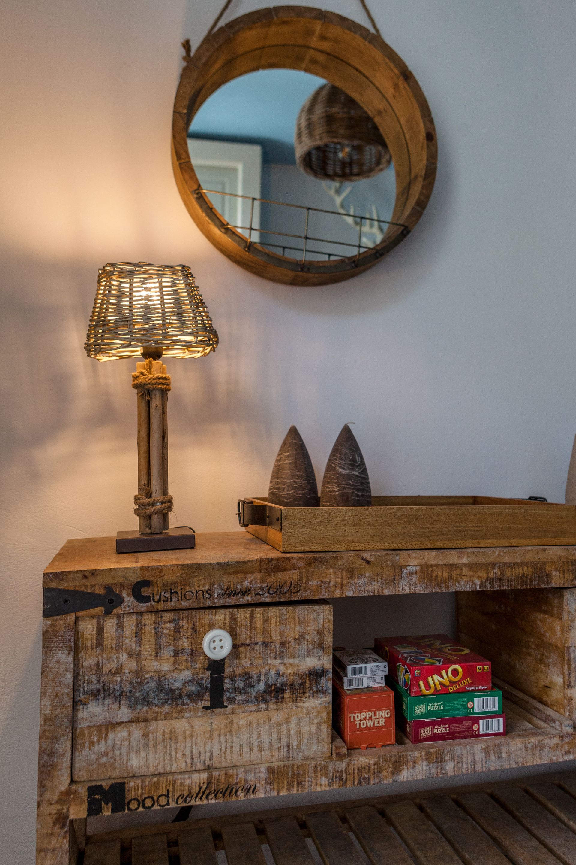 A wooden console table with a lamp, a mirror, and some board games.