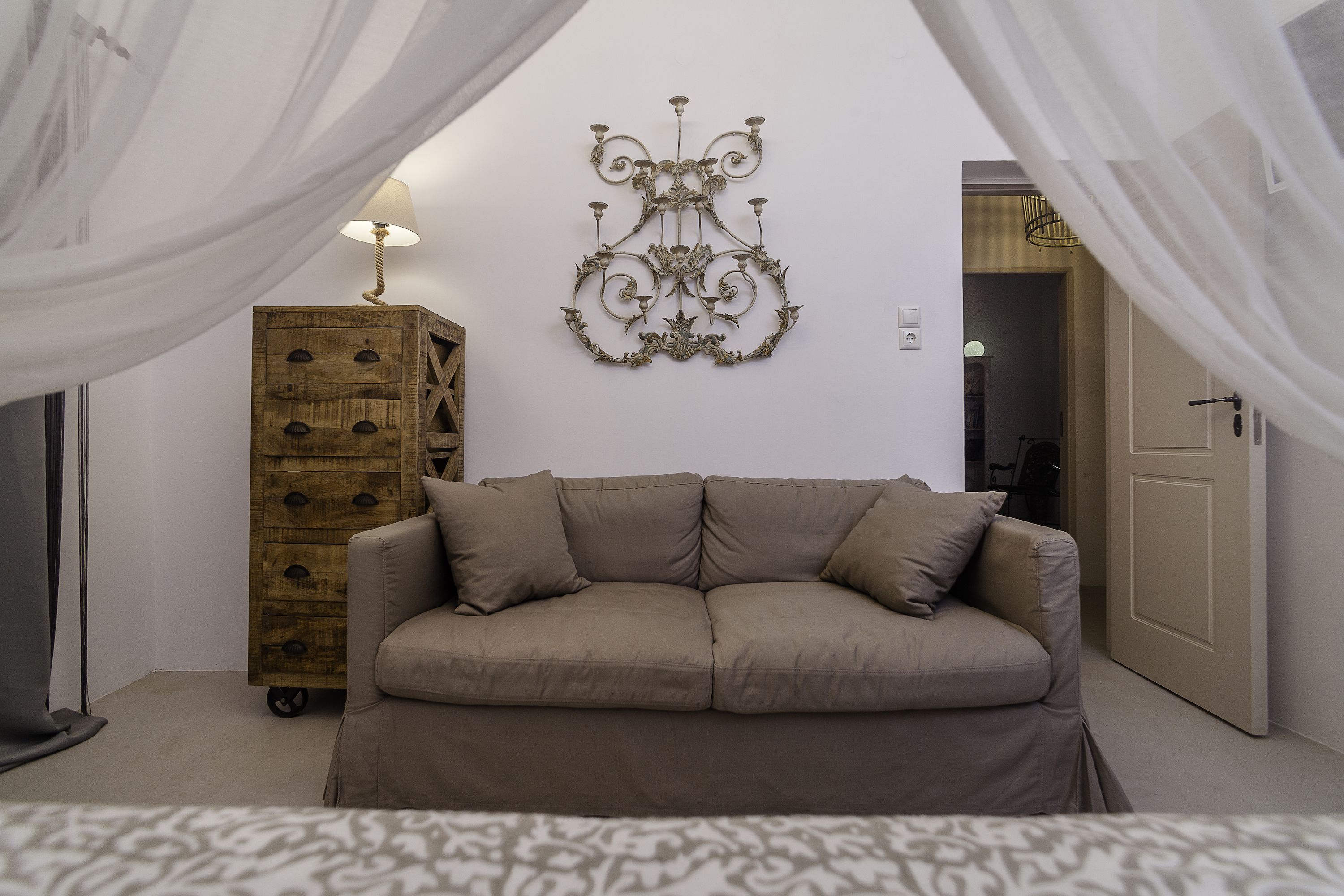 A bedroom with a beige sofa, a wooden chest of drawers, and a wall-mounted light fixture.