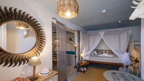 A bedroom with a canopy bed, a round table, a mirror with a sunburst frame, and a bedside lamp.