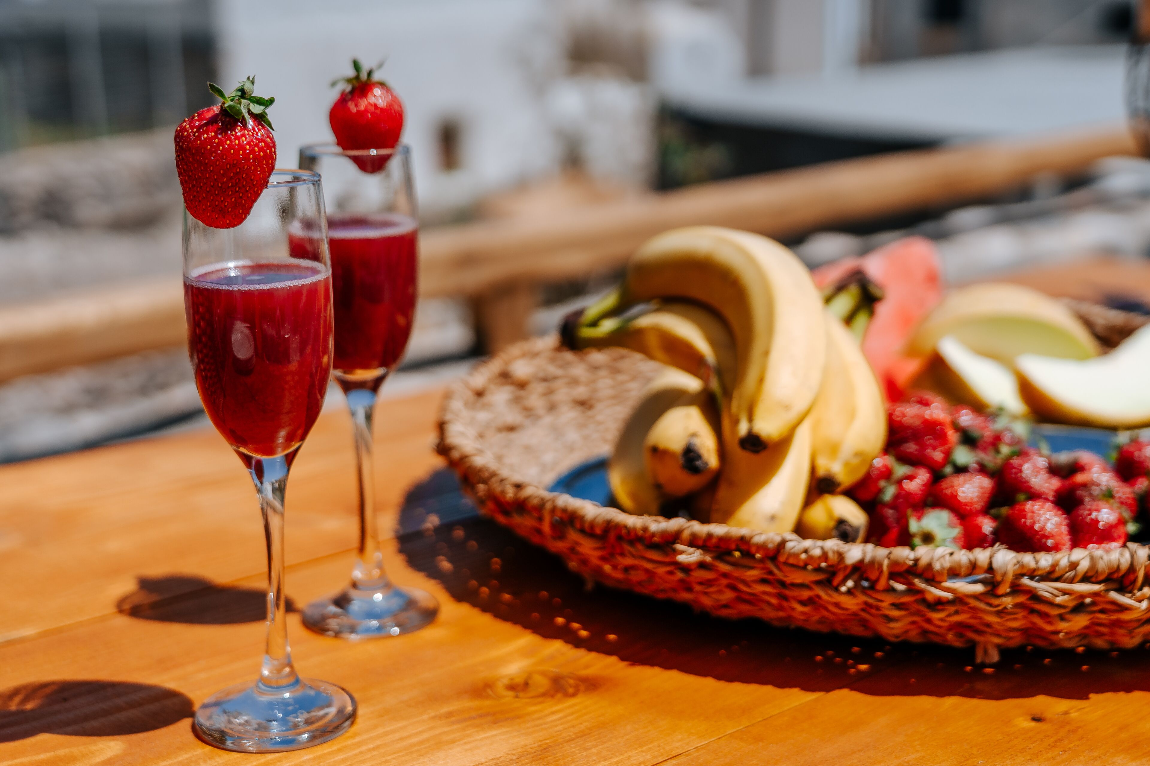 A wooden table with two glasses of red beverage, a basket of fruits, and a banana.