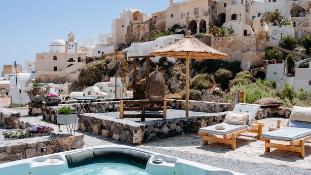 A hot tub with lounge chairs and a wooden gazebo, surrounded by white buildings with domed roofs.