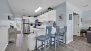 A modern kitchen with white cabinetry, a stainless steel refrigerator, and a breakfast bar with blue chairs.