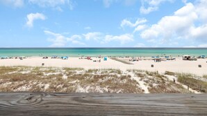 A beach with a wooden deck in the foreground, sandy beach, and a clear blue sky.